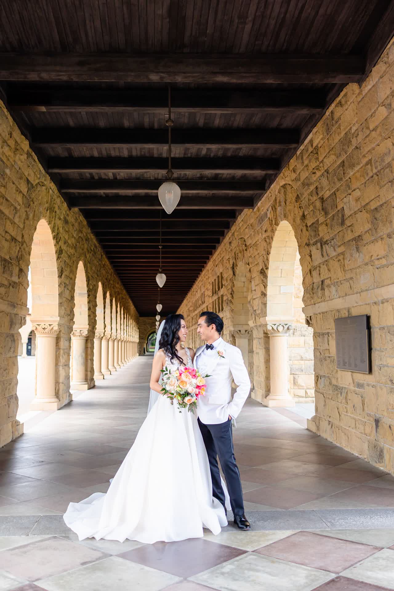 Couple standing beneath stone arches with wedding bouquet